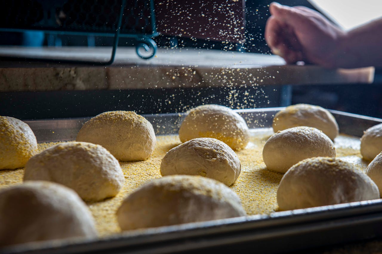 Home Close-up of dough balls in a bakery setting, ready for baking with a sprinkle of flour.