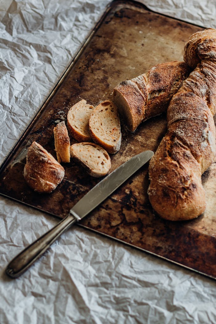 Home Freshly baked rustic bread loaf with slices on a textured baking tray.