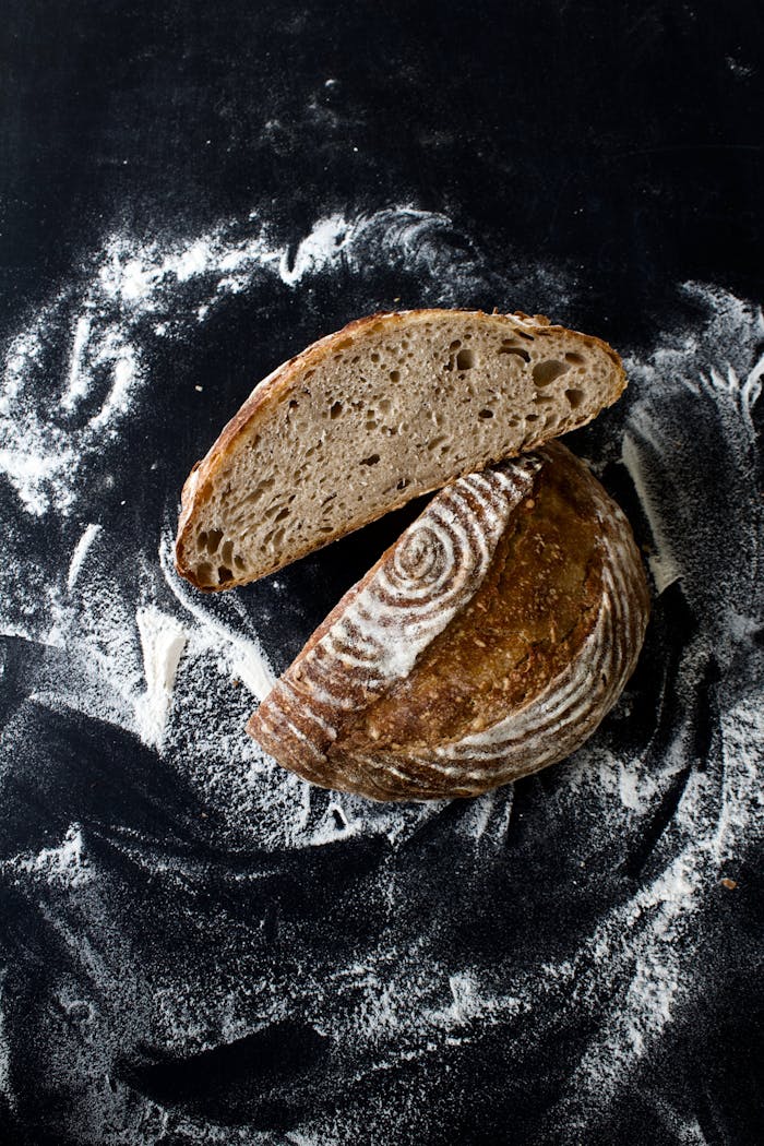 Offerings Top view of sliced sourdough bread on a black table covered with flour.